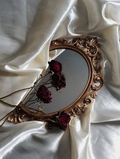 a mirror sitting on top of a bed covered in white sheets and satin material with dried flowers