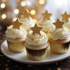 cupcakes with white frosting and gold stars on top sitting on a plate