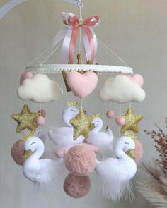 a pink and white mobile with stars, clouds and swans hanging from it's sides