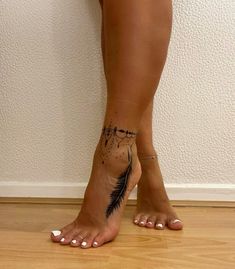 a woman's foot with a feather tattoo on it, standing in front of a wall