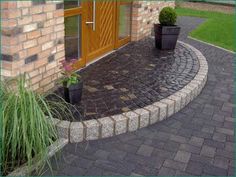 a brick walkway with potted plants next to the front door and side entryway