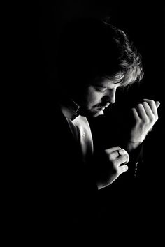 black and white photograph of a man in the dark with his hands clasped to his chest