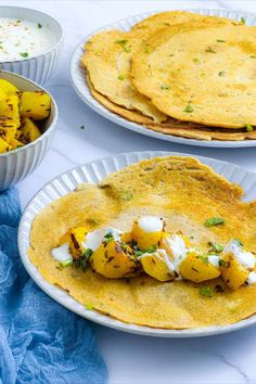 Red lentil pancakes on a white plate with potatoes and raita in the background.