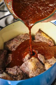 someone is pouring sauce on some meat in a blue pot that has been cooked for dinner