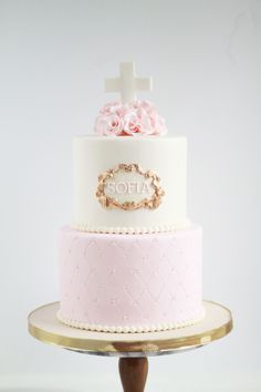 a three tiered cake with pink flowers and a cross on the top is shown