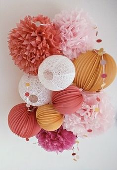 there is a bunch of paper flowers hanging on the wall with balls and pom poms