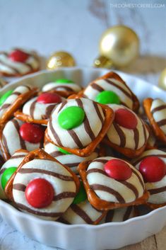 small white bowls filled with candy covered pretzels on a table next to christmas ornaments