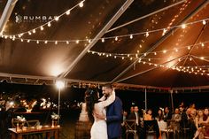 a bride and groom share their first dance under a tent at night with string lights