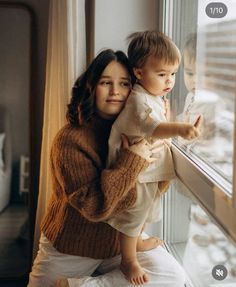 a woman holding a small child looking out the window at something in front of her