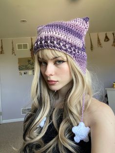 a woman with long blonde hair wearing a purple knitted cat ear flap beanie