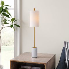 a table with a lamp on it in front of a window and a bookcase