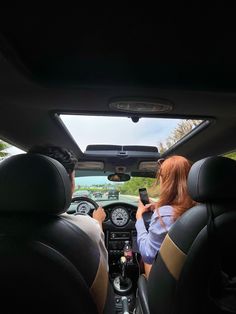 two people sitting in the driver's seat of a car looking at their cell phones