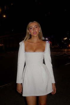 a woman in a white dress is standing on the street at night with her hands behind her back