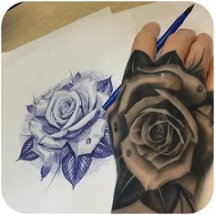 a hand holding a pencil next to a drawing of a black and white rose on paper