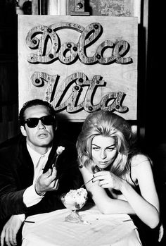 a man and woman sitting at a table eating ice cream in front of a sign