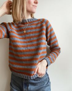 a woman standing in front of a white wall wearing a striped sweater and blue jeans