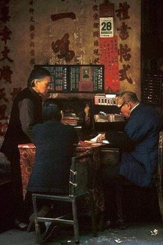 two people sitting at a desk in front of a book shelf with books on it