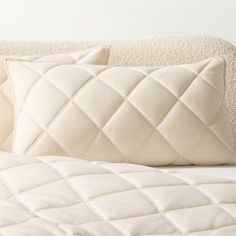 a white bed with two pillows on top of it and a pillow in the middle