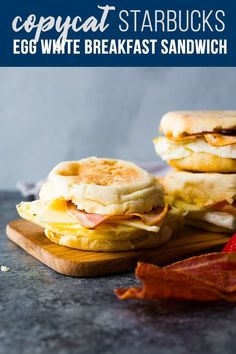 two eggs and bacon breakfast sandwiches on a cutting board with bacon in the foreground