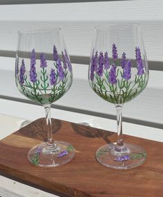 two wine glasses sitting on top of a wooden table with purple flowers painted on them