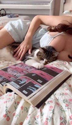 a woman laying in bed next to a cat on top of a book with an open page