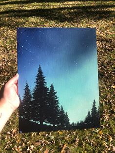 a hand holding up a card with trees and stars in the night sky on it