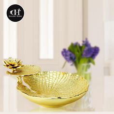 two golden bowls sitting on top of a white table next to purple and yellow flowers