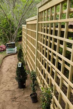 a wooden fence in the middle of a dirt path with potted plants on either side