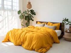 a bed with yellow sheets and pillows in a white room next to a potted plant