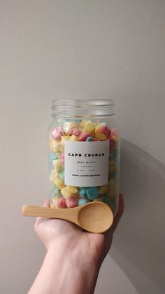 a hand holding a jar filled with gummy bears and a wooden spoon next to it