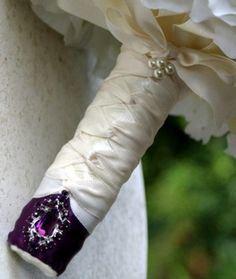 the bridal bouquet is adorned with purple and white ribbon, beads and pearls on it