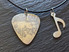 a guitar pick and musical note pendant on a black leather cord with a music note charm attached to it