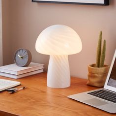 a laptop computer sitting on top of a wooden desk next to a mushroom shaped lamp