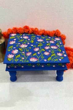 a blue ottoman with flowers on it next to a potted plant and tin can