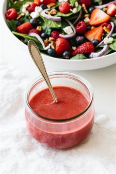 a salad with strawberries and spinach is in a bowl next to a spoon