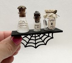 three miniature bottles on a shelf with spider webs attached to the top and bottom