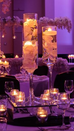 two tall glass vases filled with water and lit candles on top of a table