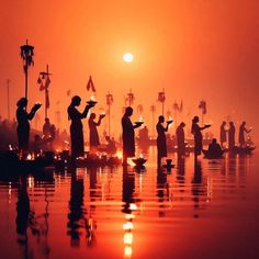 silhouettes of people standing in the water at sunset or dawn with their hands together