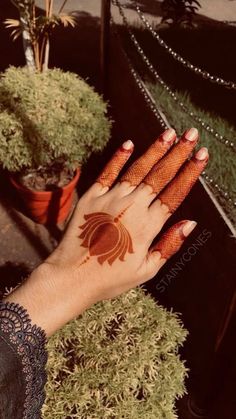 a woman's hand with hennap on it and some potted plants in the background