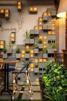 a table and chairs in front of a wall with lit plants on the outside,