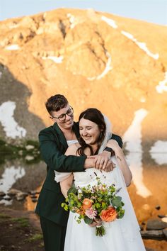 a bride and groom hugging each other in front of a mountain