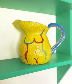 a yellow pitcher sitting on top of a green shelf next to a white and blue wall