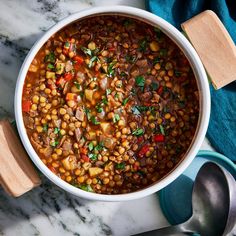 a white bowl filled with beans and vegetables on top of a marble table next to spoons