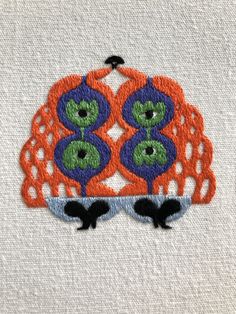 an orange and blue owl with green eyes on it's face is embroidered onto a white piece of cloth