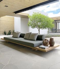 a couch sitting on top of a stone floor next to a tree and potted plant