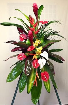 an arrangement of tropical flowers and greenery on a stand