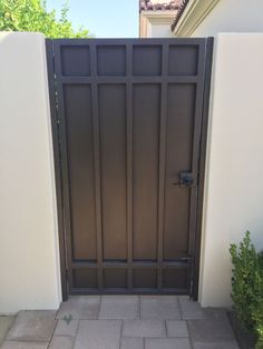 an iron gate in front of a white wall and brick walkway leading to a house