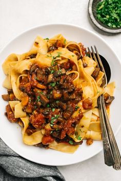 a white plate topped with pasta covered in mushroom bolognzoe next to a fork