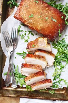 sliced pork and greens on a tray with fork, knife and napkin next to it