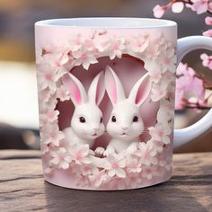 two white rabbits sitting in the middle of a pink coffee mug with cherry blossoms around them